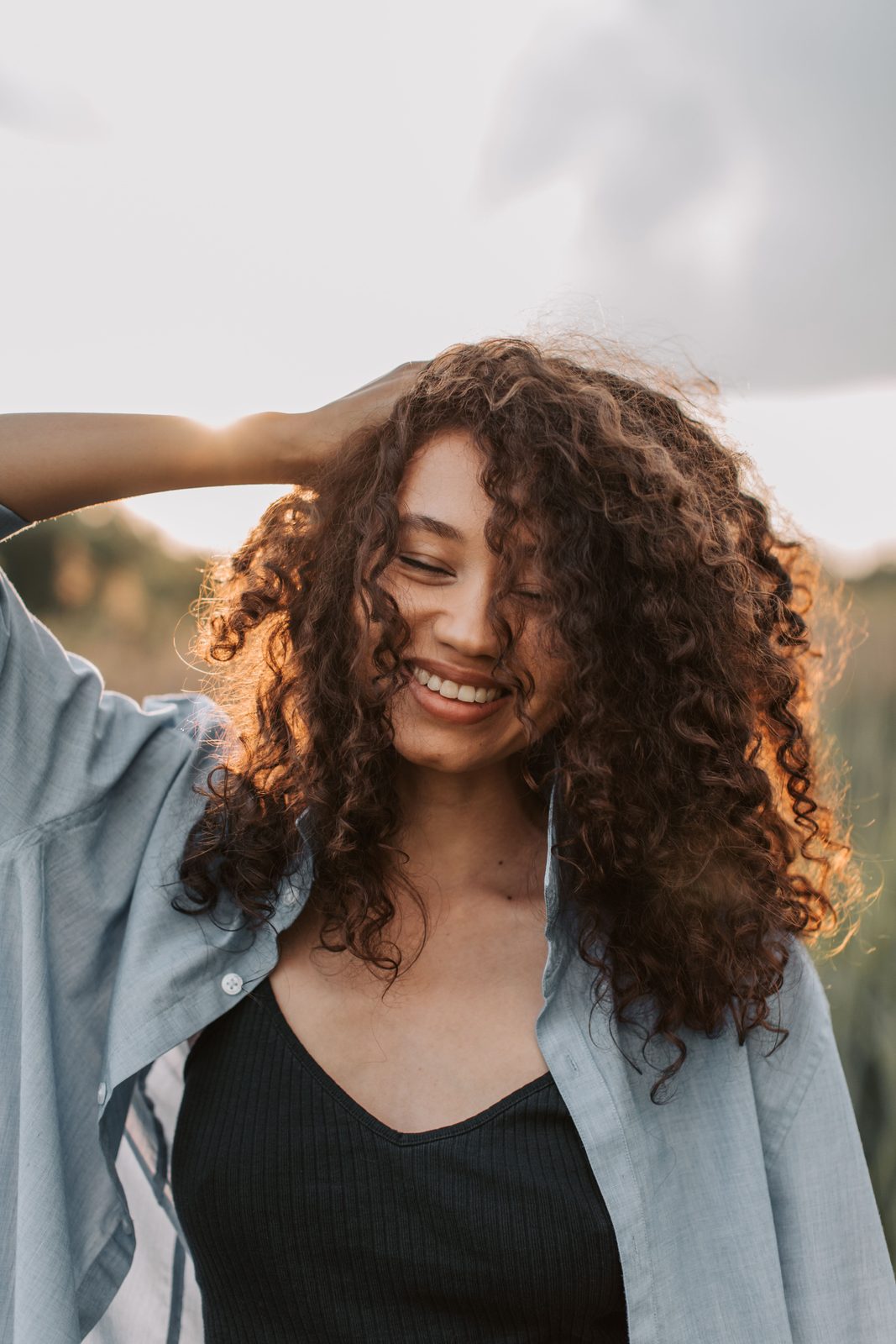 A woman smiling outdoors in warm evening light, feeling at ease