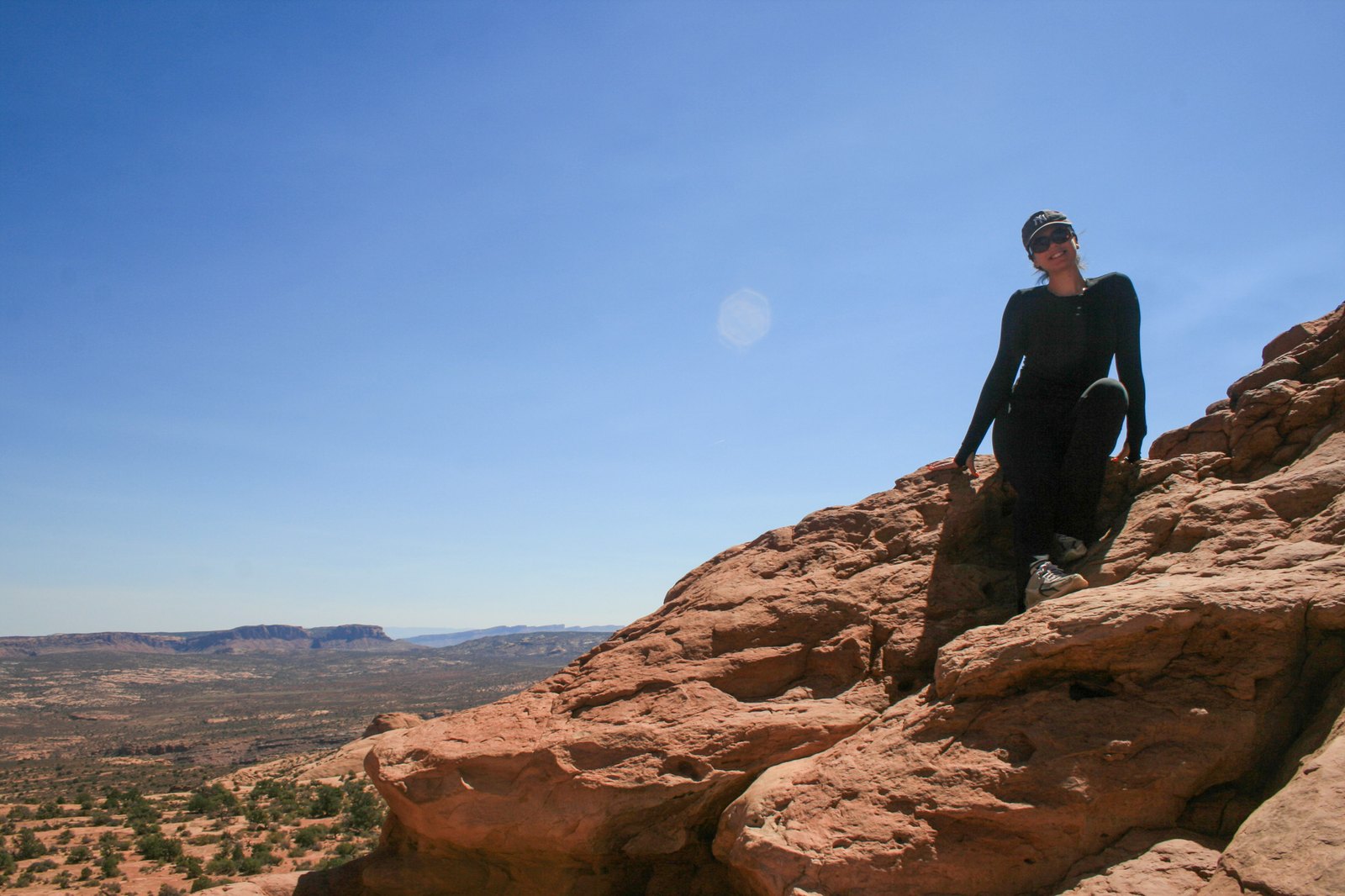 Ally sitting on red rock outcrops on a hike, with a desert view behind her