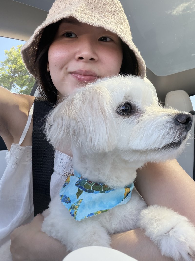 Kathleen in a car on a sunny day, holding her small white dog
