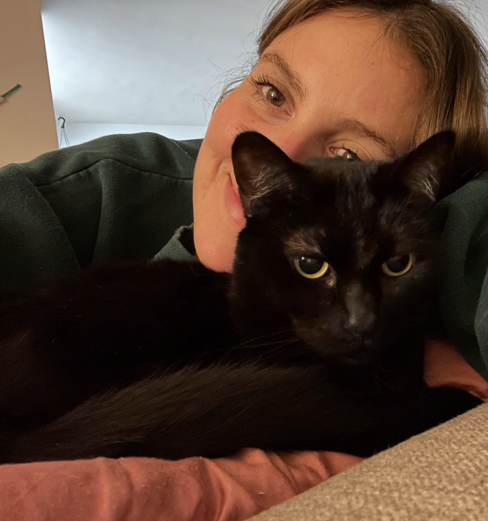 Kristina resting on the couch with her black cat