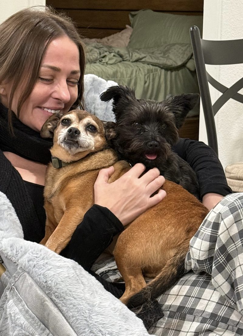 Stephanie smiling with her two dogs curled up on her lap