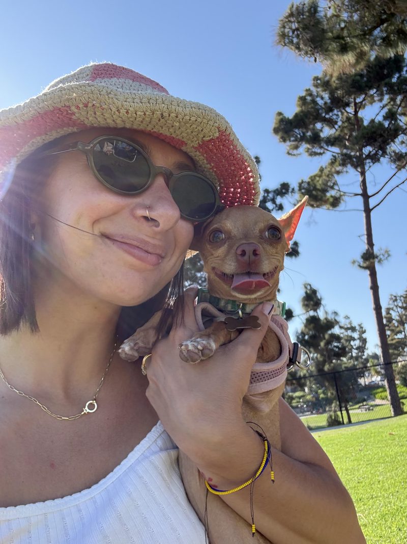 Victoria outdoors in a sun hat, holding her small dog Poppy